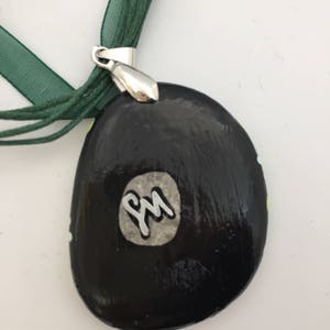 May include: Black and green painted stone pendant with a silver metal bail and a white circle with the initials "PM" in silver lettering.