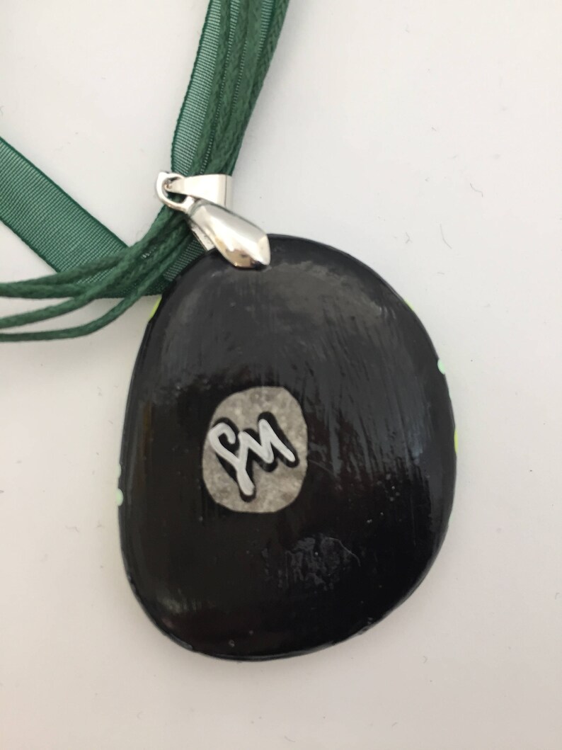 May include: Black and green painted stone pendant with a silver metal bail and a white circle with the initials "PM" in silver lettering.