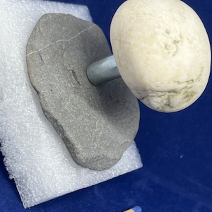 May include: A white stone mushroom sculpture with a grey stone base and a metal stem. The sculpture is sitting on a white foam surface.