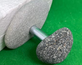 May include: A gray stone knob with a silver metal rod attached to a gray stone base. The knob is attached to a white surface.