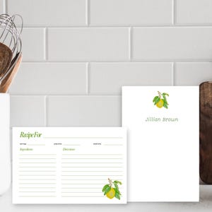 May include: A white recipe card with green lines and the text "Recipe For" at the top. The card has a lemon illustration in the bottom right corner. A white notepad with the text "Jillian Brown" in green text and a lemon illustration in the top right corner.