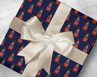 May include: A wrapped gift with navy blue wrapping paper featuring a repeating pattern of toy soldiers in red and gold. The gift is tied with a cream-colored satin ribbon and bow. A roll of matching wrapping paper is visible.