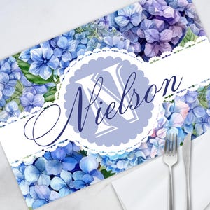 May include: Blue floral placemat with a white lace border and a monogrammed initial "N" in a circle with the name "Nielson" written in cursive.