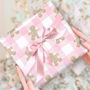 Peut inclure: Un cadeau emball&eacute; dans du papier &agrave; motifs vichy rose avec des bonhommes en pain d'&eacute;pices. Il est nou&eacute; avec un ruban et un n&oelig;ud en satin rose. Le th&egrave;me g&eacute;n&eacute;ral est festif et li&eacute; aux f&ecirc;tes.