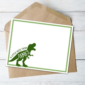 May include: A white stationery card with a green border and a green dinosaur graphic. The text "A little note from James" is printed on the card. The card is inside a brown envelope.