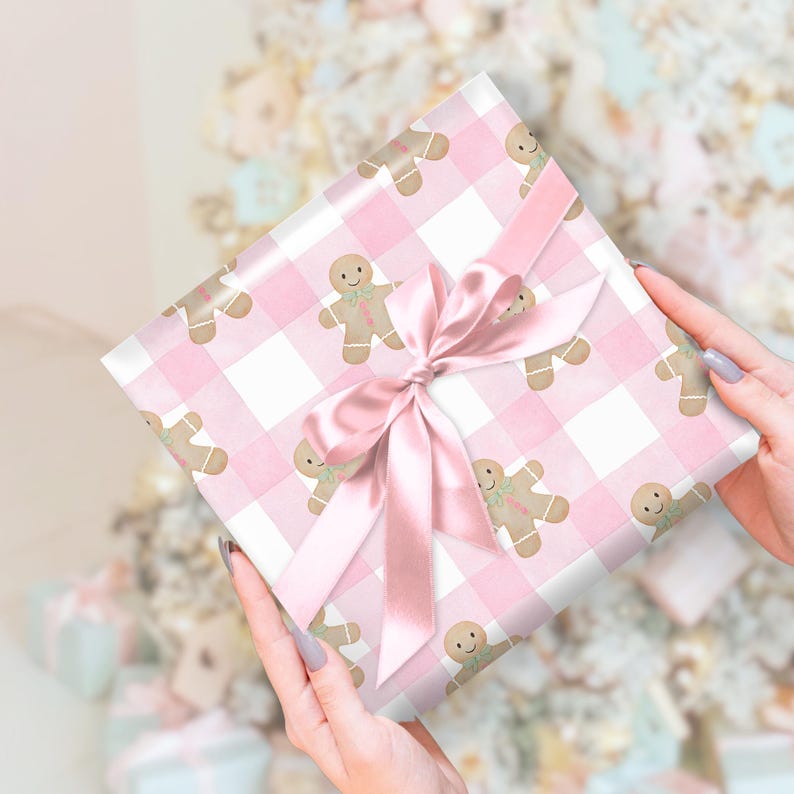 Peut inclure: Un cadeau emball&eacute; dans du papier &agrave; motifs vichy rose avec des bonhommes en pain d'&eacute;pices. Il est nou&eacute; avec un ruban et un n&oelig;ud en satin rose. Le th&egrave;me g&eacute;n&eacute;ral est festif et li&eacute; aux f&ecirc;tes.