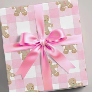 Peut inclure: Un coffret cadeau emball&eacute; avec un motif vichy rose et des bonhommes en pain d'&eacute;pices. Un grand ruban de satin rose est nou&eacute; en n&oelig;ud. Le papier d'emballage est id&eacute;al pour No&euml;l ou une baby shower. La bo&icirc;te est de forme carr&eacute;e.