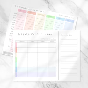 May include: Two white paper planners. The top planner is labeled "3:3:3: productivity planner" with color-coded sections for each day of the week. The bottom planner is a "Weekly Meal Planner" with a shopping list section.