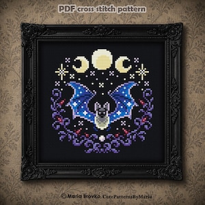 May include: A PDF cross stitch pattern featuring a central bat with blue wings adorned with white stars, surrounded by a purple floral wreath and celestial moon phases in yellow, all set against a black background within a black ornate frame.