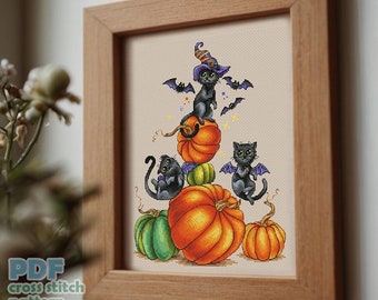 May include: Cross stitch pattern featuring three black cats wearing witch hats and wings, perched on top of a stack of pumpkins. The pumpkins are orange, green, and purple. The background is a white canvas.