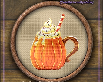 Può includere: Modello di punto croce di un latte alla zucca con panna montata e una cannuccia rossa e bianca. Il motivo è in un telaio da ricamo in legno.
