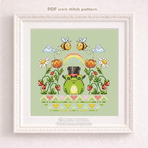 May include: Cross-stitch pattern in a white frame featuring a green frog wearing a top hat, surrounded by flowers, bees, and a rainbow. The text "PDF cross stitch pattern" is at the top. The design includes strawberries and a decorative border.