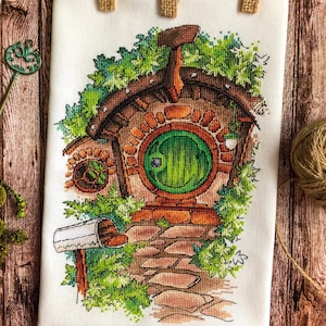 Puede incluir: Patrón de punto de cruz de una casa hobbit con una puerta redonda verde, rodeada de vegetación y un camino de piedra. La casa está hecha de ladrillo marrón y tiene un techo marrón.