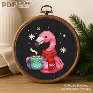 May include: A cross-stitch pattern of a pink flamingo wearing a red scarf, holding a teal mug of coffee, and surrounded by snowflakes. The design is set against a black background within a wooden embroidery hoop. The text "PDF cross stitch pattern" is at the top.