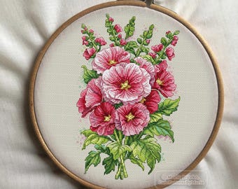 May include: A cross-stitch embroidery hoop with a floral design of pink hollyhocks with green leaves and stems. The design is on a white background. The text "Cross Stitch Patterns by Maria" is in the lower right corner.