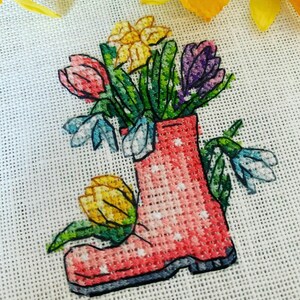 May include: A pink rubber boot with white polka dots filled with a bouquet of flowers. The flowers include yellow daffodils, pink tulips, purple crocuses, and blue snowdrops.