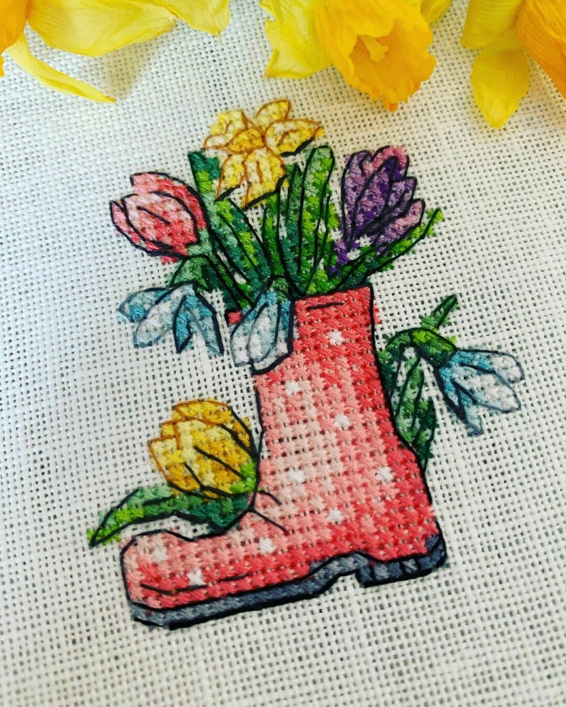 May include: A pink rubber boot with white polka dots filled with a bouquet of flowers. The flowers include yellow daffodils, pink tulips, purple crocuses, and blue snowdrops.
