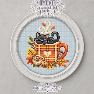Könnte beinhalten: Ein PDF-Kreuzstichmuster mit einer schwarzen Katze, die in einer orange-gelben Tasse mit Karomuster und weißem Herz ruht. Das Design zeigt Dampf, Herbstblätter, eine Zimtschnecke und einen Keks, eingefasst in einem weißen kreisförmigen Rahmen.
