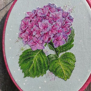 May include: A close-up of a pink and purple hydrangea flower with green leaves, embroidered on a light blue fabric.