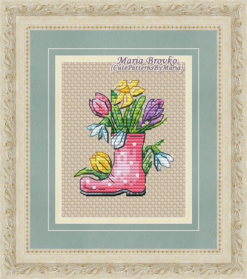 May include: A pink rubber boot with white polka dots filled with a bouquet of colorful flowers, including yellow daffodils, purple crocuses, and white snowdrops. The boot is sitting on a beige background. The text "Maria Brovko (CutePatternsByMaria)" is written above the boot.