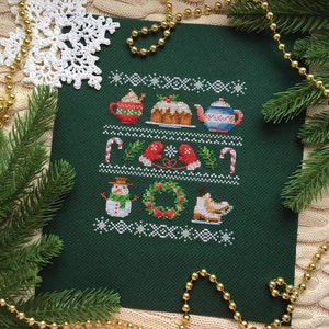 Puede incluir: Un patrón de punto de cruz verde con un tema navideño de invierno. El patrón incluye un muñeco de nieve, una corona, una tetera, un bastón de caramelo, guantes y una casa de jengibre.