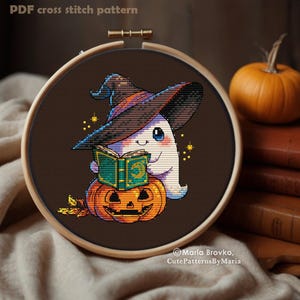 May include: A cross-stitch pattern in a wooden hoop features a cartoon ghost wearing a witch hat and reading a book while sitting on a carved pumpkin. The text "PDF cross stitch pattern" is at the top. The design includes gold stars and autumn leaves.