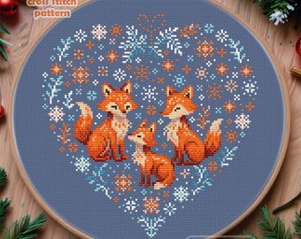 Puede incluir: Patrón de punto de cruz con un diseño en forma de corazón con tres zorros y copos de nieve sobre un fondo azul. El patrón se titula "Cute Patterns by Maria".