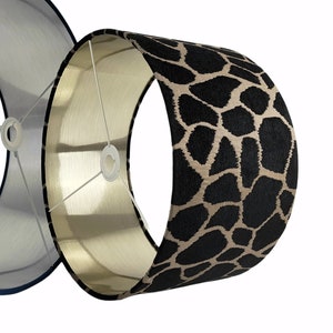 May include: A black and beige lampshade with a giraffe print pattern. The lampshade is made of fabric and has a gold lining.