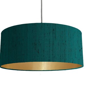 May include: A teal blue drum lampshade with a gold inner lining. The lampshade is made of a textured fabric.