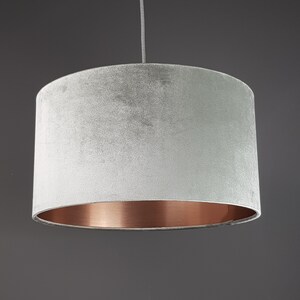 May include: A gray velvet lampshade with a copper bottom edge. The lampshade is hanging from a ceiling fixture.