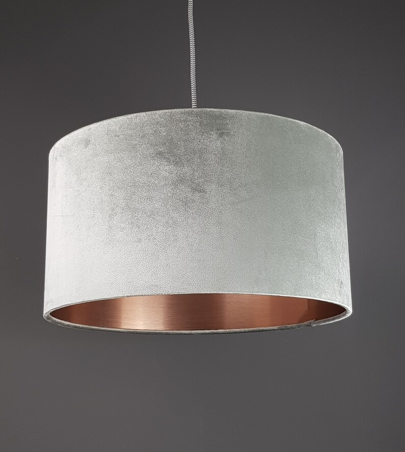 May include: A gray velvet lampshade with a copper bottom edge. The lampshade is hanging from a ceiling fixture.