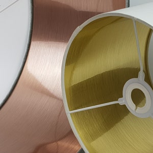 May include: Three lampshades with different colored metallic finishes. The lampshades are white on the inside and have a brushed metal finish on the outside. The lampshades are in shades of rose gold, gold, and silver.