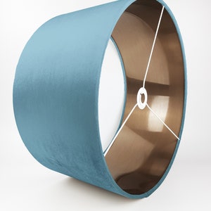 May include: A teal blue velvet lampshade with a copper lining. The lampshade is cylindrical and has a white cord.