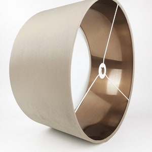 May include: A beige lampshade with a copper lining. The lampshade is cylindrical and has a smooth, fabric-like texture.