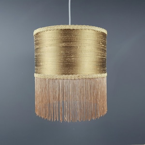 May include: A gold lampshade with a fringe trim. The lampshade is cylindrical and has a gold fabric covering.