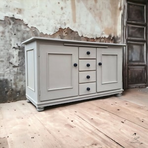 May include: A light grey wooden cabinet with two doors and five drawers. The cabinet has dark blue knobs and sits on a wooden floor.