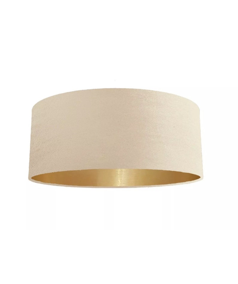 K&ouml;nnte beinhalten: Ein cremefarbener Lampenschirm mit goldfarbenem Metallic-Besatz. Der Lampenschirm ist aus Stoff und hat eine glatte, gleichm&auml;&szlig;ige Textur.
