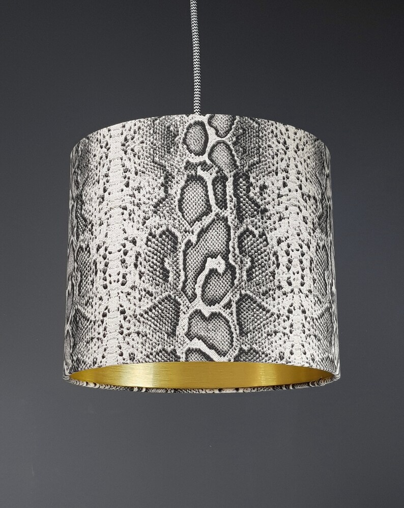 May include: A black and white snake skin patterned lampshade with a gold trim.