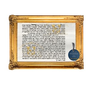 May include: A framed print of a Hebrew text in black ink on a white background. The frame is gold and ornate. A small tag with the text "Hebrew ArtDesigns" is attached to the bottom right corner of the frame.