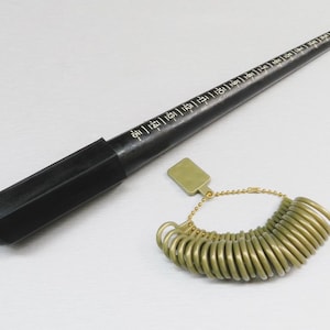 May include: A black ring sizer mandrel with size markings and a set of gold-colored ring sizer gauges. The mandrel is a cone shape, and the ring sizers are attached to a chain with a tag.