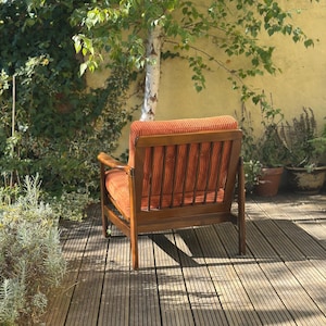 Pu&ograve; includere: Una poltrona in velluto a coste arancione con struttura in legno. La sedia &egrave; posizionata su un terrazzo in legno, con un albero e vegetazione sullo sfondo. Le dimensioni della sedia sono di circa 76 cm di larghezza, 81 cm di profondit&agrave; e 86 cm di altezza.