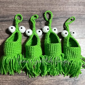 May include: Five crocheted green monster-shaped hanging baskets with white eyes and a fringe bottom.