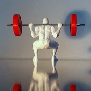 Può includere: Una statuetta bianca di una persona che solleva un bilanciere con pesi rossi. La persona è in posizione di squat con le braccia distese sopra la testa.