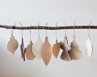 Könnte beinhalten: Eine Sammlung von Holz-Weihnachtsschmuck in verschiedenen Formen, darunter Tropfen, Sterne und ein Weihnachtsbaum, die an einem natürlichen Ast hängen. Die Ornamente sind aus hellen und dunklen Holztönen gefertigt und mit Schnur aufgehängt.