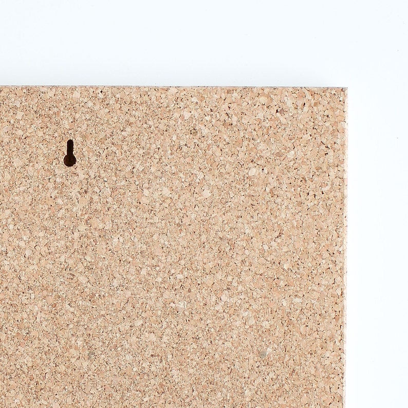 May include: A close-up of a corkboard with a small hole in the top left corner. The corkboard is a light brown color and has a rough texture.