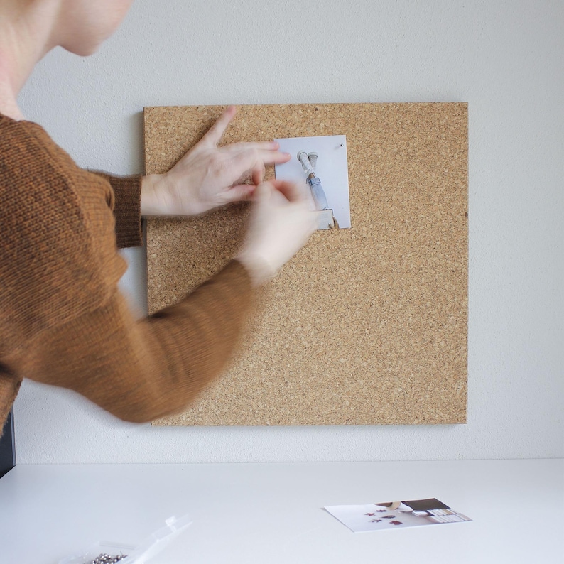 May include: A person pinning a photo to a corkboard. The photo shows a person's legs and feet in the air. The corkboard is brown and has a rough texture.