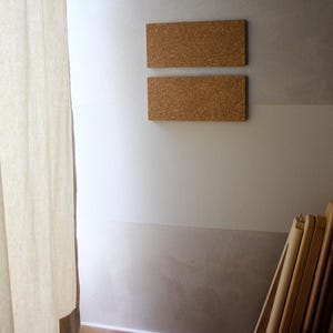May include: Two rectangular cork boards mounted on a white wall with a light brown lower section. The boards are stacked vertically, with the top board slightly higher than the bottom board.