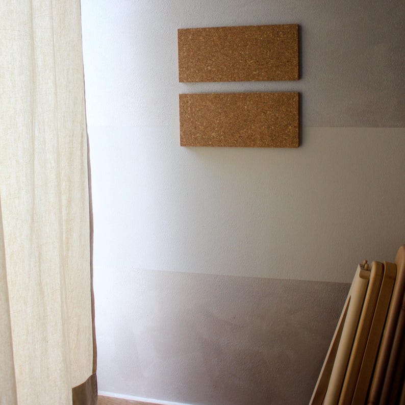May include: Two rectangular cork boards mounted on a white wall with a light brown lower section. The boards are stacked vertically, with the top board slightly higher than the bottom board.