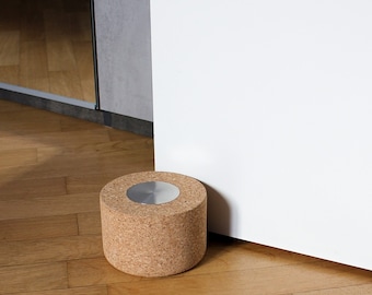 May include: A round cork doorstop with a silver metal top. The doorstop is sitting on a wooden floor.