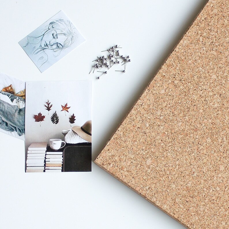May include: A corkboard with a stack of books, a mug, a hat, and fall leaves pinned to it. There are also push pins scattered around the corkboard.